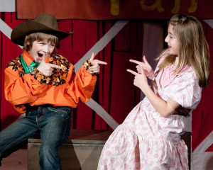 Two children actors in costume pointing at eachother while dressed in western clothing.